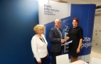 Na zdjęciu na biało-niebieskim tle napis: Punkt informacyjny funduszy europejskich. Przed tłem stoją trzy osoby: dwie kobiety, pomiędzy nimi mężczyzna - Jerzy Sirak.
