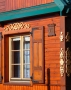 zdjęcie przedstawia fragment drewnianego domu z oknem i okiennicami, nad oknem umieszczona jest drewniana ornamentyka