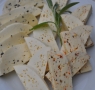 zdjęcie przedstawia rozłożone na talerzu kawałki białego sera z dodatkami przypraw, ozdobiony listkiem rozmarynu