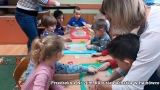 Na zdjęciu dzieci siedzą przy stolikach. Na nich trzy tace z rozwałkowanym ciastem.