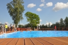 osoby kąpią się w większym basenie; błekitna woda komponuje się z brązem drewnianego podestu