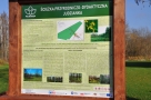 jedna z tablic edukacyjnych, ustawiona na ścieżce; tablica ma drewniane obramowanie, na częci mertytorycznej dominuje kolor zielony, zawiera ona opis roślnnosci oraz zdjęcia