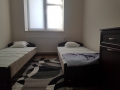 Pokój z dwoma łóżkami, pomiędzy nimi dywan, na końcu pokoju okno.