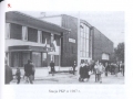skan czarno-białego zdjęcia, na którym widoczni są podróżujący, stojący na peronie przed wejściem do budynku dworca
