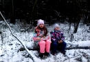 dwie dziewczynki siedzące na pniu leżącym w lesie; wokół ziemia przykrta jest białą warstwą śniegu