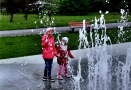 dwie małe dziewczynki stoją przy wytrysującej fontannie w Parku Miejskim