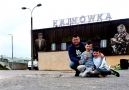 dwóch chłopców wraz z ojcem pozują przykucnięci na tle budynku dawnego dworca; widoczna jest ściana z muralem starszego mężczyzny i kobiety oraz duży napis Hajnówka na dachu