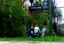 dwaj chłopcy i ich ojciec stoją przy kierunkowskazie kierującym na Kolejki Leśne przy Nadleśnictwie Hajnówka