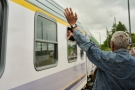 Fragment pociągu odjeżdżającego z peronu, z prawej strony mężczyzna stojący tyłem z ręką uniesioną w górę, machający odjeżdżającym.