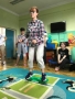 kobieta stoi na zielonym urzędzeniu do ćwieczenia blanasu; za nią siedzą pozostali uczestnicy