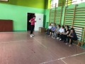 w sali gimnastycznej na ławce siedzi grupa osób przed nimi stoi trenerka