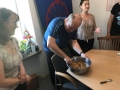 trzy osoby, mężczyzna stoi przy stole i wyrabia w misce potrawę, obok niego stoją dwie kobiety