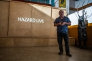 mężczyzna stojący na tle ściany z lty, na które wyślietlony jest napis Hazard Live