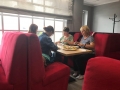 Uczestnicy wycieczki siedzą na czerwonych kanapach wokół stołu i jedzą