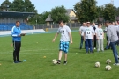 Na murawie stoją zawodnicy, jeden z nich kopie piłkę.