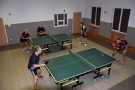 Na zdjęciui dwa stoły do gry w tenisa stołowego, czterech uczestników gra, jedna osoba siedzi na krześle