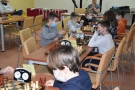 Dzieci siedzą przy stole naprzeciw siebie i grają w szachy.