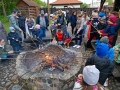 Dzei i dorośli pieką kiełbaski przy ognisku