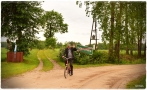 rowerzysta na drodze polnej. W tle widać znak drogowy z nazwą wsi.