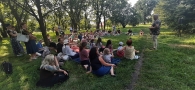 Mężczyzna przemawia do publiczności siedzącej na trawie.