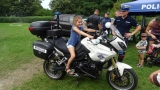 Dziewczynka siedzi na motocyklu policyjnym, obok stoi umundurowany policjant.