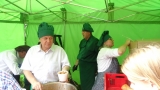 Burmistrz Miasta ubrany w białą koszulę i zielony czepek kucharski nalewa zupę.