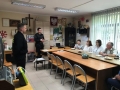 Pięciu uczestników spotkania siedzi przy stole, po lewej stronie stoi dwóch strażaków.