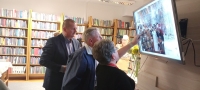 trzy osoby stoją przed telewizorem, na którym wyświewtlane jest stare zdjęcie