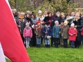 Delegacja dzieci i nauczycieli stojących przed pomnikiem w parku, składających kwiaty.