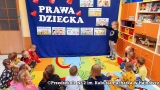 Dzieci siedzą na podłodze, przed nimi granatowe tło z napisem: Prawa dziecka