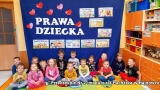 Dzieci siedzą na podłodze, za nimi granatowe tło z napisem: Prawa dziecka