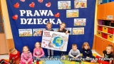 Dzieci siedzą na podłodze, za nimi granatowe tło z napisem: Prawa dziecka