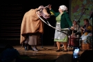 starsza kobieta w chustce trzyma za lejce przebraną za krowę osobę