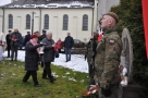 Kobieta składa wiązankę , mężczyzna trzyma znicz. Z prawej strony stoi żołnierz na warcie.