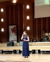 dziewczyna w długiej granatowej sukni stoi na scenie. W dłoni trzyma mikrofon.