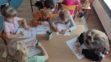Dzieci siedzą przy stolikach i kolorują figury.