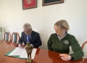 Burmistrz podpisuje umowę, obok niego siedzi Prezes Fundacji, na stole przed nimi stoi miniatura pomnika, 