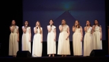 dziewczęta z zespołu w białych sukniach śpiewają na scenie