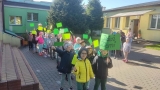 Przedszkolaki z zielonymi flagami w rękach idą w kierunku parku miejskiego. 