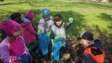 Dzieci zaopatrzone w rękawiczki i worki sprzątają teren parku.