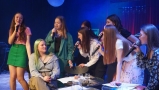 Dziewczyna siedzi przy stoliku. Inne śpiewają dla niej. Sceneria jak w kawiarni.