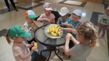 Dzieci siedza pryz stoliku. Na talerzu leżą banany.