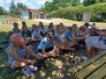 Dzieci siedzą i leżą na kocach w ogrodzie przedszkolnym, słuchają czytanych przez panie książek.