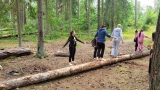 dzieci i dorośli na boso przecjodzą po leżącym drzewie