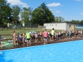 Uczestnicy dtoją przy brzegu basenu podczas rozpoczęcia zawodów.