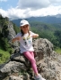 Dziewczynka w koszulce oparta o skałę. W tle widać góry.