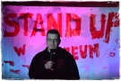 mężczyzna z mikrofonem. W tle widać podświetlony napis STAND UP 