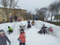 Na podwórku dzieci bawią się na górce, zjeżdżają na pupach, robią anioły na śniegu, biegają po placu. 