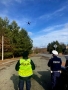 dwóch policjantów stoi przy drodze i sterują dronem, ktory wzniósł się w powietrze