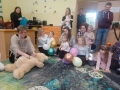 pani wykonuje masaż dla misia. Obok przyglądają się dzieci i opiekunowie. Dzieci trzymają balony.